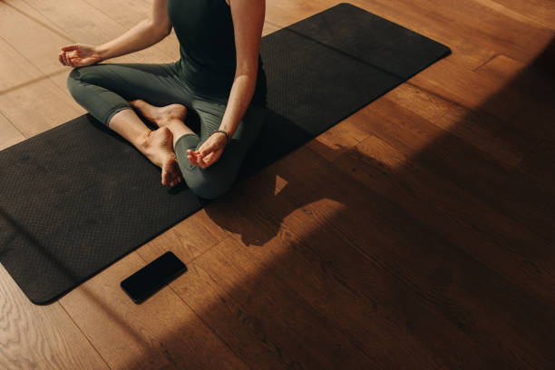 Personne assise en tailleur sur un tapis de yoga, sur un parquet ensoleillé